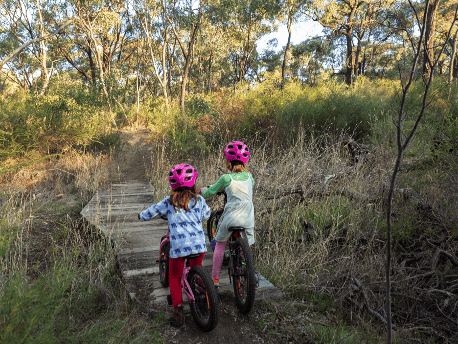 Young girls on bikes about to cross a wooden bridge